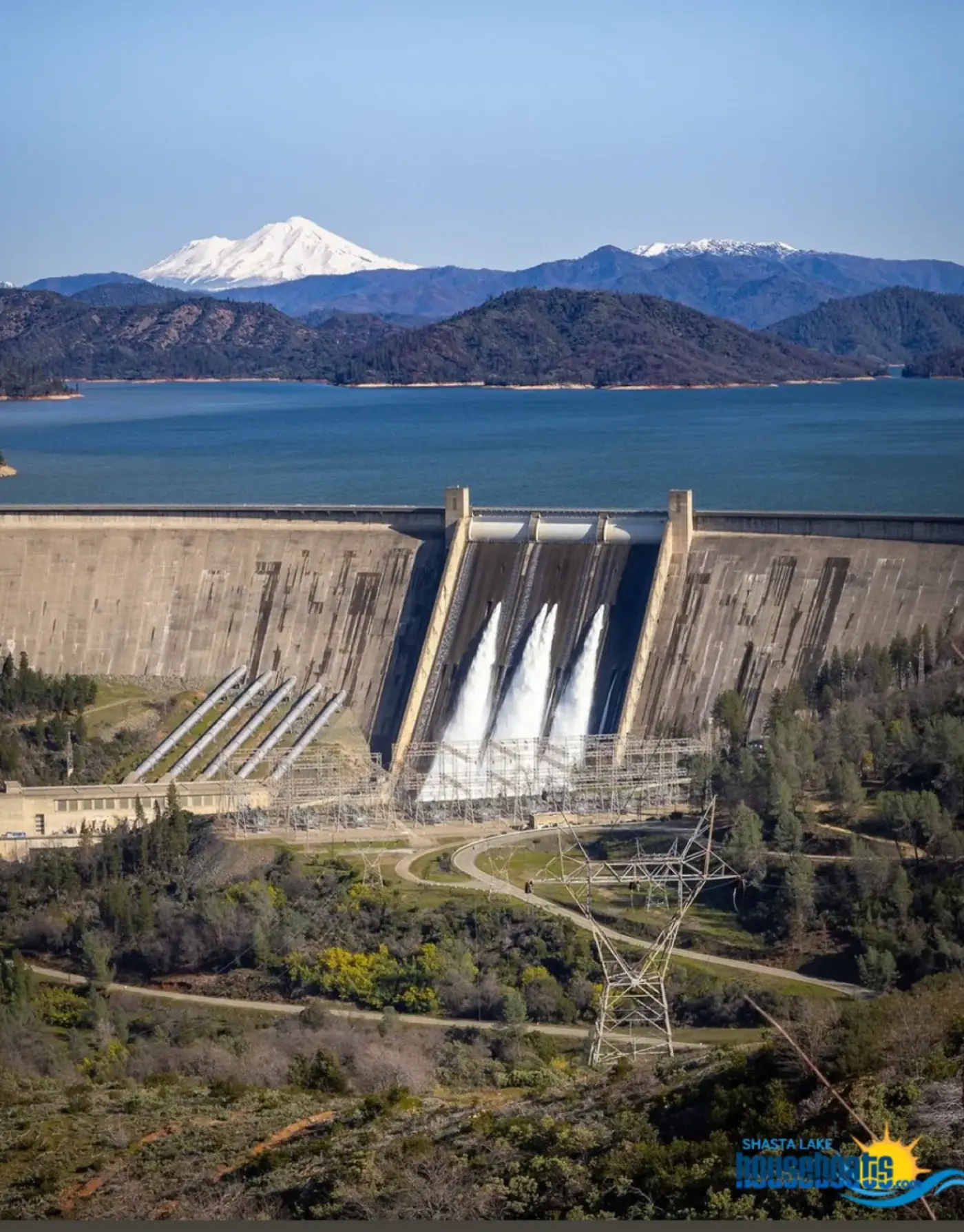 Shasta Dam releasing water with Shasta Lake and snow-capped Mount Shasta in the background